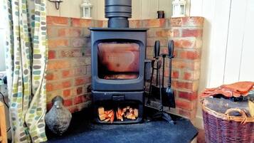 A wood-burning stove with a brick wall and a basket to the right.