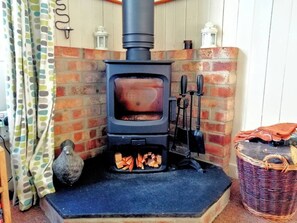 A wood-burning stove with a brick wall and a basket to the right.