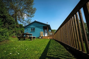 A blue house with a wooden deck, a picnic table, and a grassy yard.