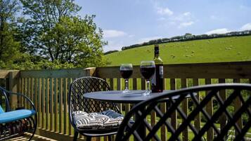 An outdoor seating area with a table and chairs, a bottle of wine, and glasses on a wooden deck.