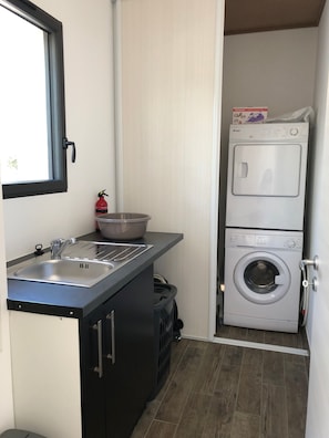 A compact laundry room with a washing machine, a sink, and a drying rack.