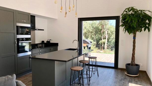 A modern kitchen with a central island, bar stools, a potted plant, and a view of the outdoors. - Villa heated pool & garden •Town center 5 min •Beaches 10 min •Cleaning included (Porto Vecchio)