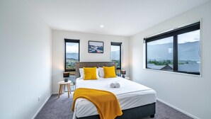 A modern bedroom with a large bed, two windows, and a view of the mountains. - Kirimoko Family Retreat (Wanaka)