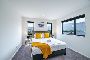Une chambre moderne avec un grand lit, deux fenêtres et une vue sur les montagnes.
