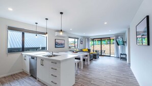 A modern kitchen with a central island, a dining area with a table and chairs, and a living space with a sofa and a TV. - Kirimoko Family Retreat (Wanaka)