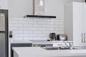 A modern kitchen with white subway tiles, a stainless steel range hood, a kettle, and a toaster.