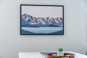 A framed artwork of mountains and a lake on a wall.