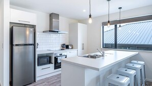 A modern kitchen with a stainless steel refrigerator, white cabinetry, a built-in oven, and a large window with a view of the roof. - Kirimoko Family Retreat (Wanaka)