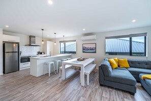 A modern kitchen with a central island, white bar stools, and a grey sectional sofa with yellow cushions.