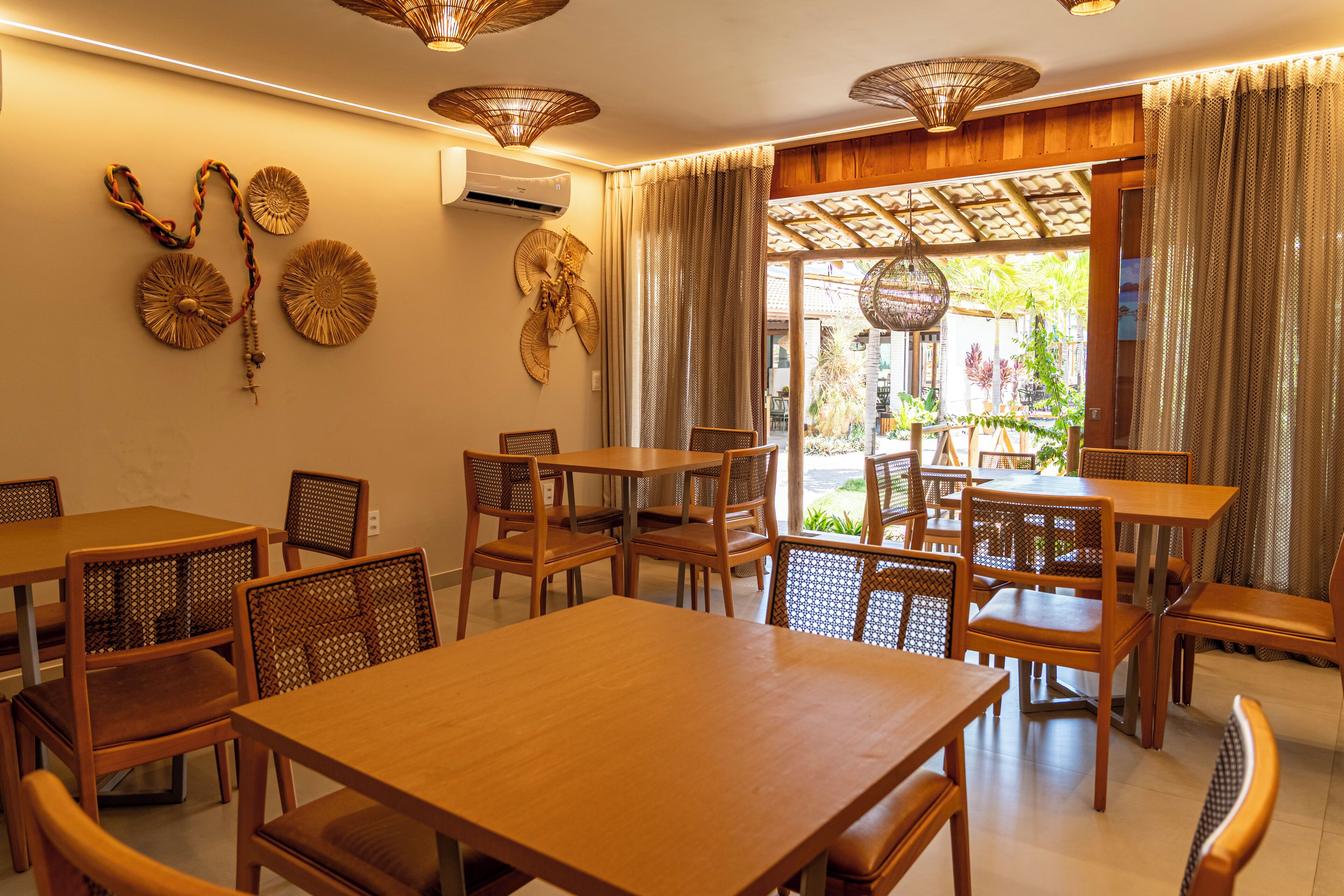A restaurant with wooden tables and chairs, woven wall decorations, and a view of the outdoors.