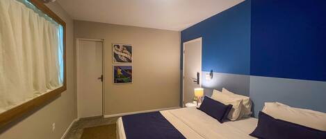 A hotel room with a bed, a bedside table with a lamp, and two paintings on the wall.