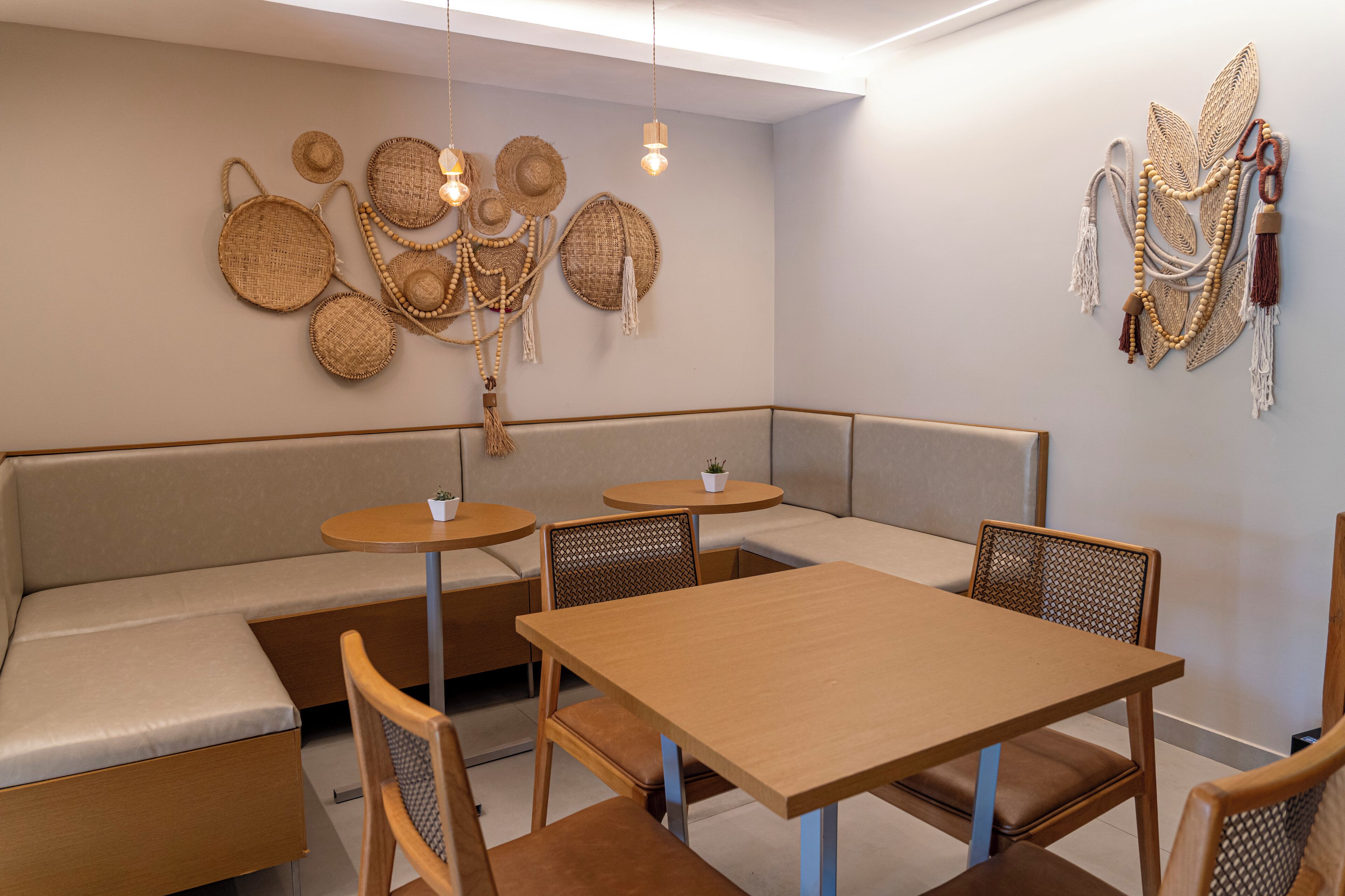 Un interior moderno con una mesa de madera y bancos, una pared decorada con cestas tejidas y joyería de cuentas, y una pequeña planta en maceta sobre una mesa redonda.
