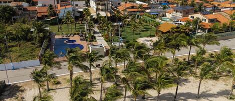 An aerial view of a coastal residential area with houses, a swimming pool, and palm trees.