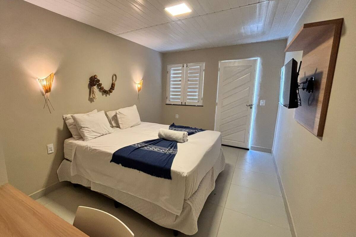 A bedroom with a bed, bedside lamps, a desk, and a door.