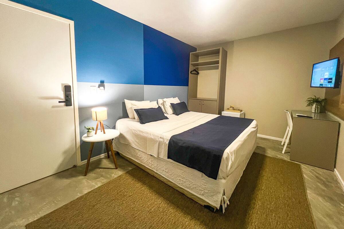 A hotel room with a bed, bedside table, lamp, and a television on the wall.