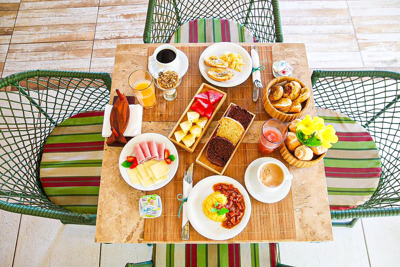 A table set with breakfast items including eggs, pastries, and beverages, surrounded by wicker chairs.