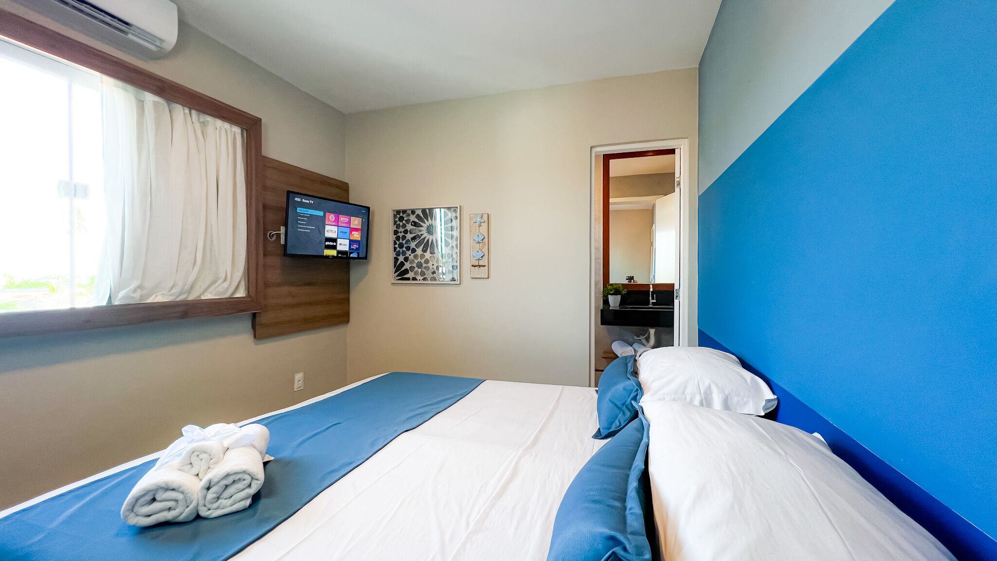 Una habitación de hotel con una cama, un televisor montado en la pared y una ventana con cortinas.