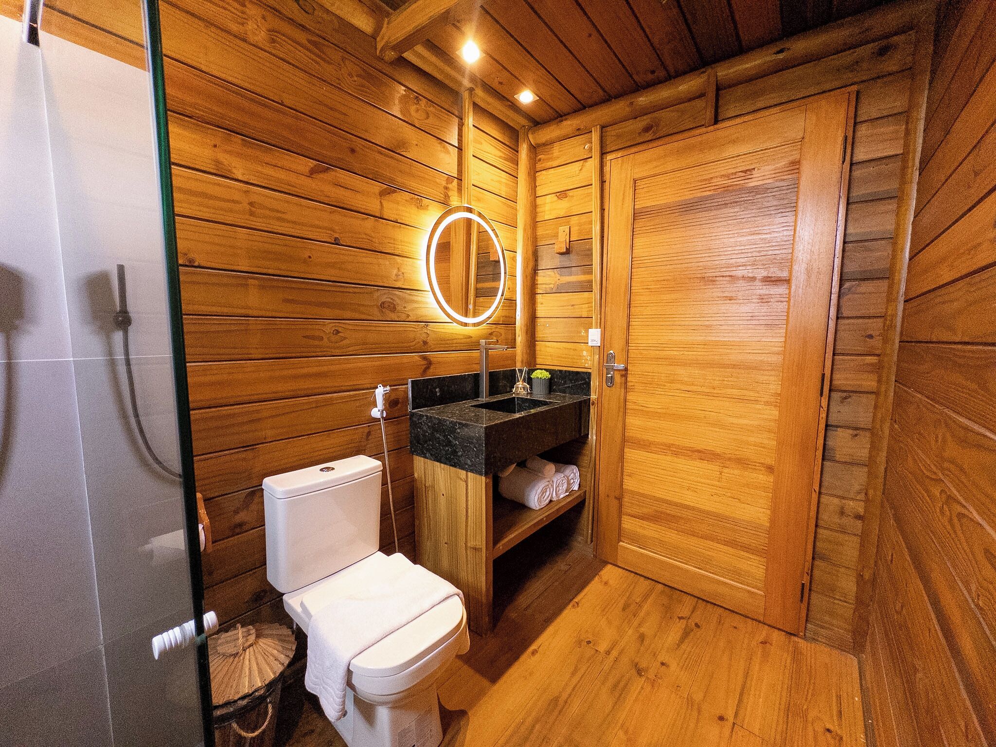 A wooden-paneled bathroom with a toilet, sink, and shower.