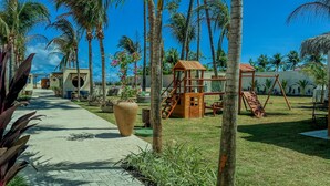 Un resort tropical con palmeras, una zona de juegos para niños y un camino que lleva a las construcciones.