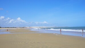 Una extensa playa de arena con olas suaves y cielo despejado.