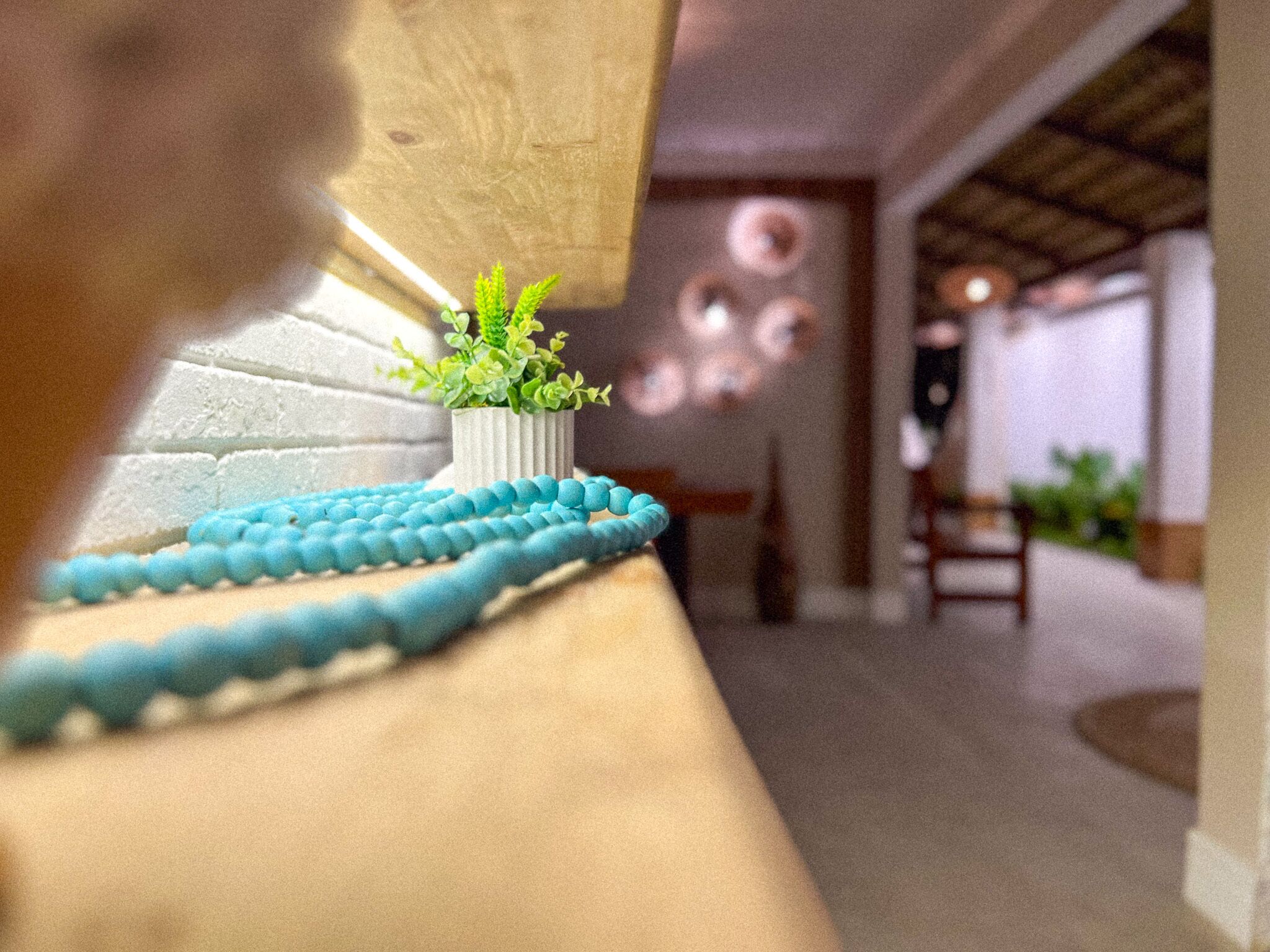 Una habitación con pared de ladrillo blanco, un pequeño jarrón blanco con plantas verdes y un borde adornado con cuentas azules.