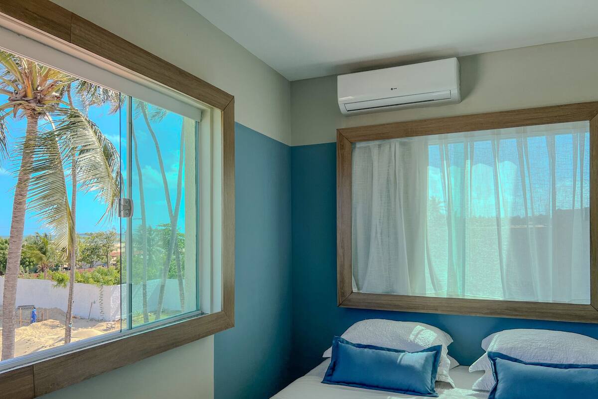 A bedroom with a bed, two pillows, a window, and an air conditioning unit.