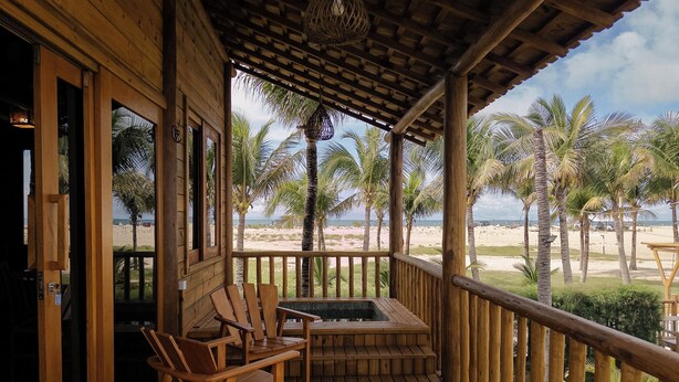 Una terraza de madera con jacuzzi, sillas y vistas a la playa.