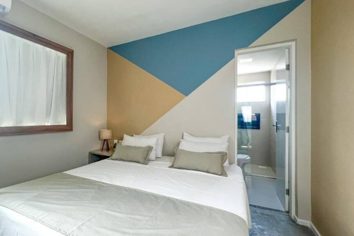 A hotel room with a bed, a nightstand, a mirror, and a door leading to a bathroom.