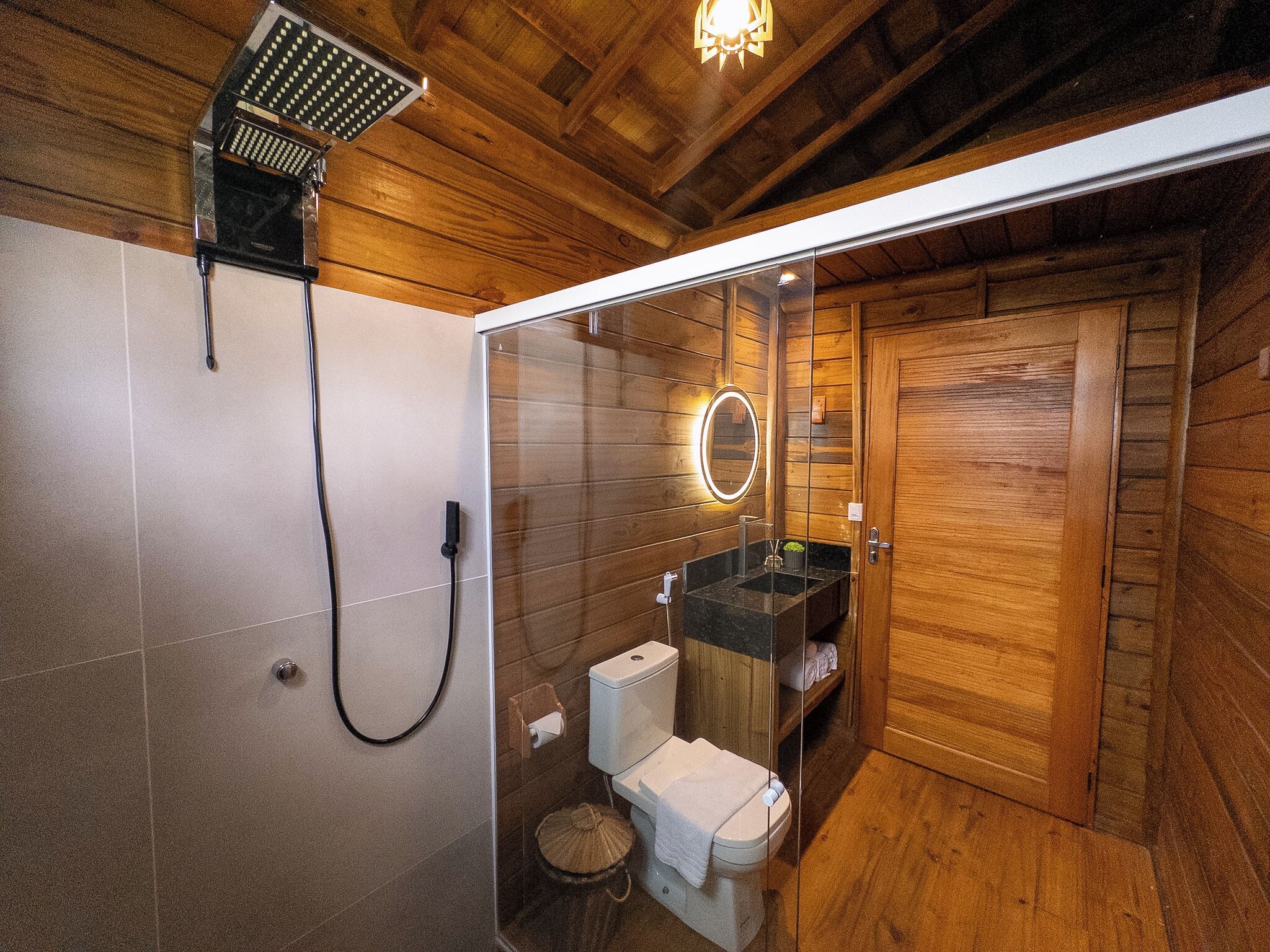 Une salle de bain aux murs lambrissés, équipée d’une douche, de toilettes et d’un lavabo.