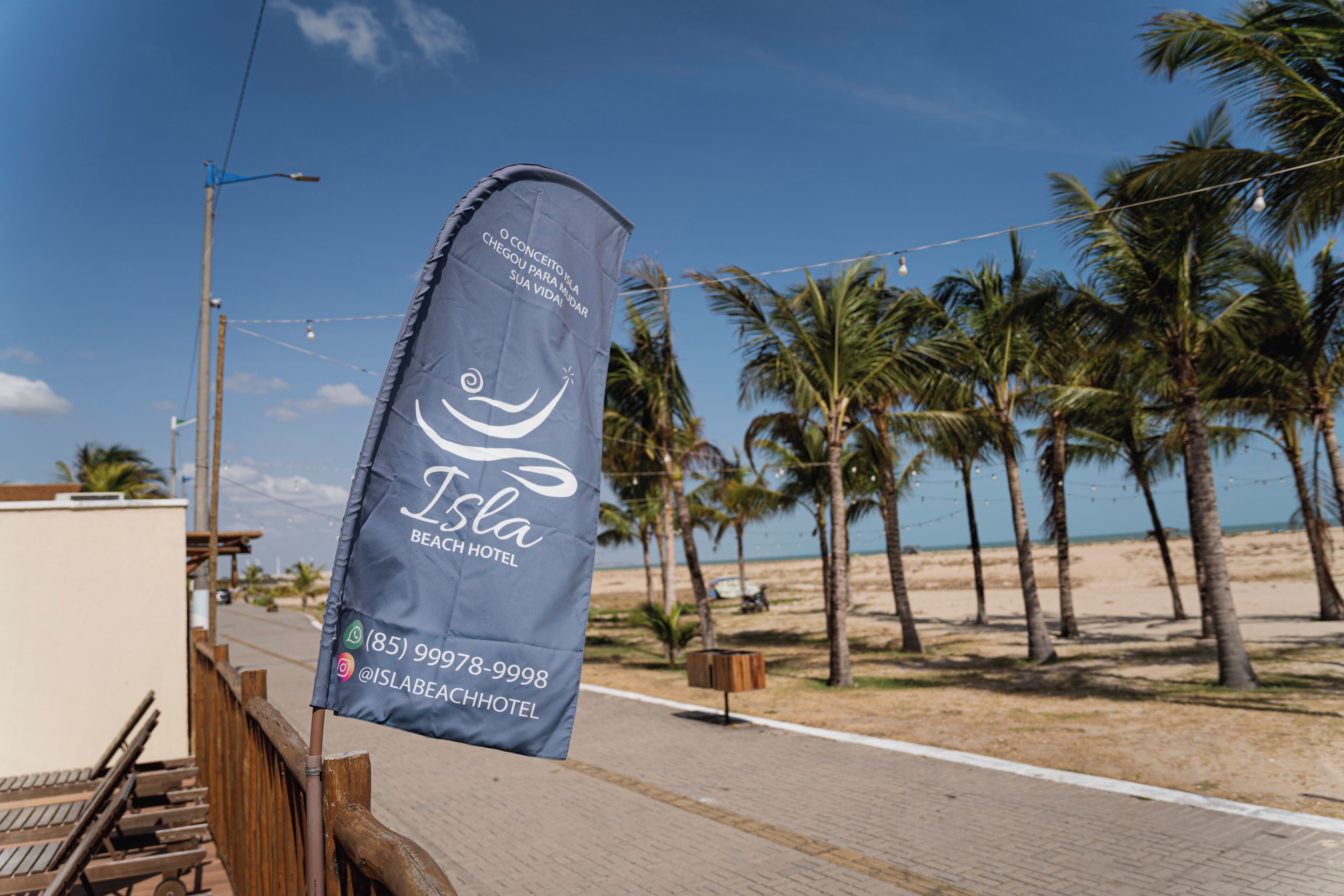 Un drapeau orné du logo et du nom de l’hôtel Isla Beach, une clôture en bois et une plage bordée de palmiers.