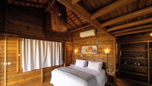Un dormitorio de cabaña de madera con una cama, una mesita de noche, un estante con vasos y una ventana con cortinas.