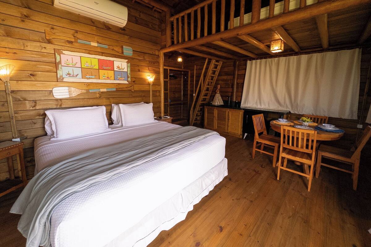 A wooden cabin room with a bed, a desk, and a chair.
