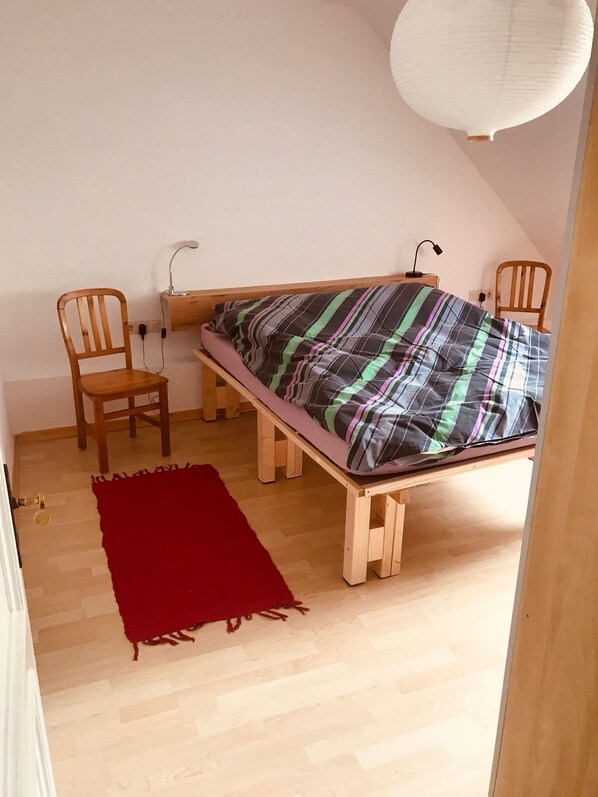 Una habitación pequeña y sencilla con una cama, una silla, un escritorio y una alfombra roja.