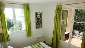 A bedroom with a bed, a radiator, a window with green curtains, and a door leading to an outdoor area. - House 8 persons 4 rooms (Coti-Chiavari)