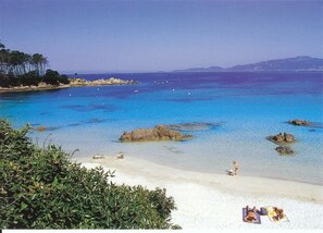 A beach with clear blue water, rocky outcrops, and a few people sunbathing.