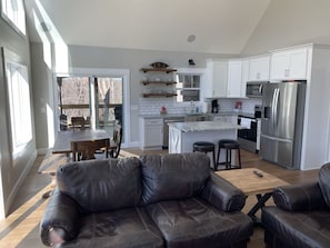 A modern kitchen with white cabinets, a stainless steel refrigerator, and a large island with stools. - Nolin Lake/Mammoth Cave Lakehouse Rental - Newly Built (Leitchfield)