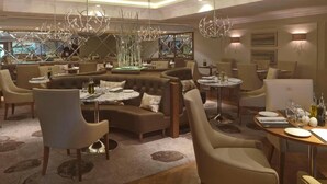 Ein modernes Restaurant mit hohen Decken, Kronleuchtern und einer gemütlichen Sitzecke mit Sofas und runden Tischen.