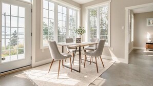 A spacious dining area with a table and chairs, large windows, and a view of greenery outside. - Stunning Ocean Front cottage, minutes from the beach (bayswater)
