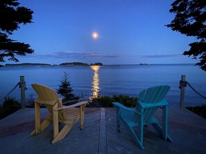 Eine Holzterrasse mit zwei Adirondack-Stühlen, die auf ein ruhiges Gewässer im Abenddämmerung blicken.