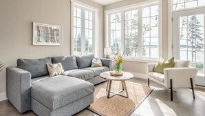 A modern living room with a grey sectional sofa, a round coffee table, and a white armchair. - Stunning Ocean Front cottage, minutes from the beach (bayswater)