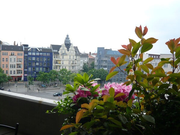 A balcony with a view of a cityscape, including multi-story buildings and a street with cars and pedestrians.