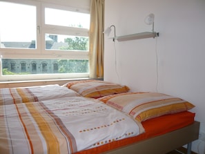 A bedroom with a bed, a window, and a wall-mounted lamp.