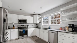 A modern kitchen with white cabinets, stainless steel appliances, a window with a view, and a countertop with various items. - Your Dynamic Retreat | Park Circle Paradise (North Charleston)