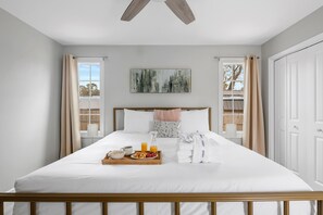 A neatly made bed with a breakfast tray, a painting on the wall, and a view of the outdoors through the window. - Your Dynamic Retreat | Park Circle Paradise (North Charleston)