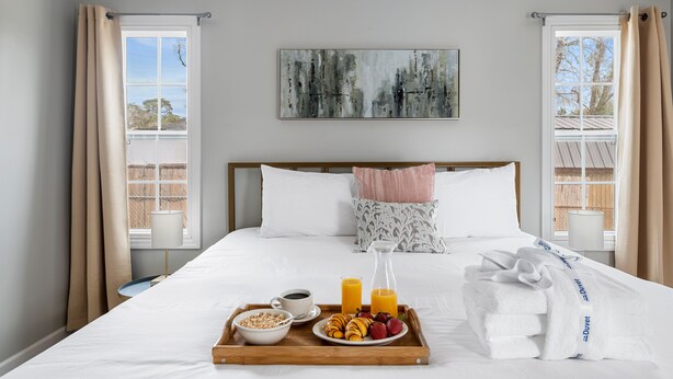 A hotel room with a bed, breakfast tray, and a painting on the wall. - Your Dynamic Retreat | Park Circle Paradise (North Charleston)