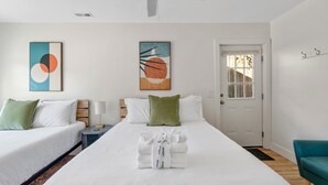 Een hotelkamer met twee bedden, een plafondventilator, kunstwerken aan de muur en een deur met een raam.