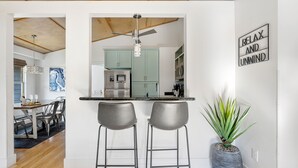 Een moderne keuken met een centraal eiland, twee barkrukken, een plafondventilator en een bordje met de tekst 'RELAX AND UNMIND'.