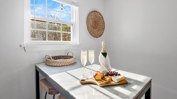 A kitchen with a marble countertop, a window with blinds, a woven basket, two glasses of champagne, a bottle of champagne, and a fruit platter. - 5 Minute Drive To The Beach! Old Village Getaway (Mount Pleasant)