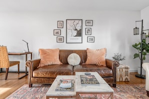 A living room with a brown leather sofa, two coffee tables, a framed map of Charleston, and a tall floor lamp.