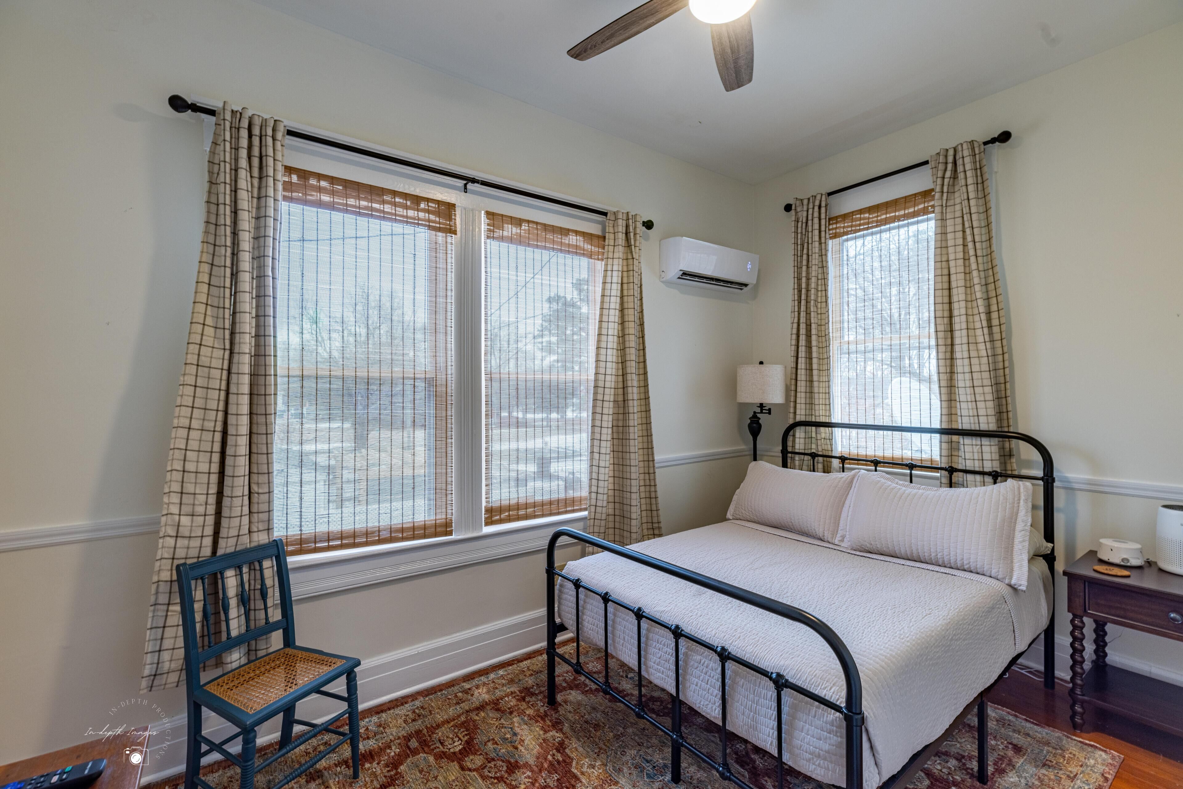 A bedroom with a bed, a chair, a window with curtains, an air conditioning unit, and a ceiling fan.